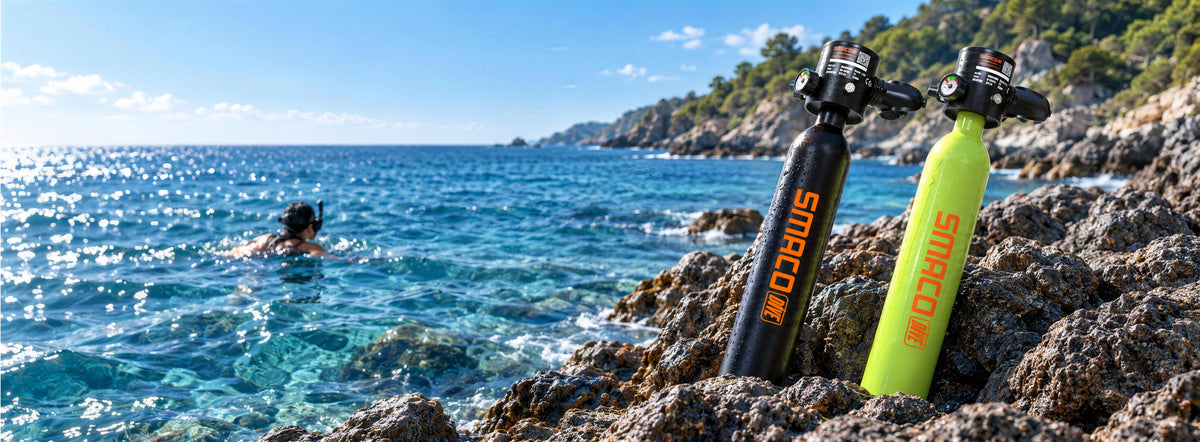 Two smaco mini dive tanks, one black and one yellow-green, displayed on rocky shore with a blue sea and sunny sky in the background.